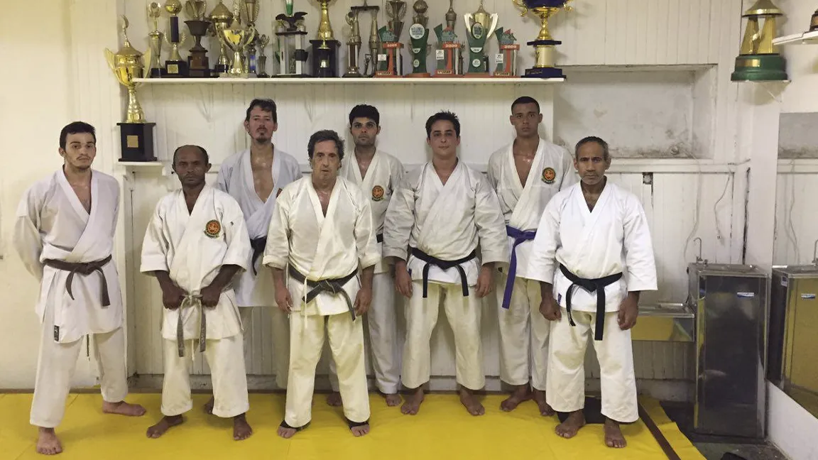 foto da Equipe de competição da Federação de Karatê-Do Tradicional do Estado do Rio de Janeiro posando junto à uma galeria de troféus