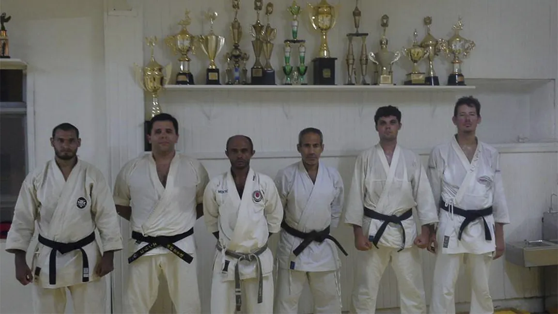 Grupo de Senseis da Academia Serrana Fight Clube posando junto à uma estante com troféus